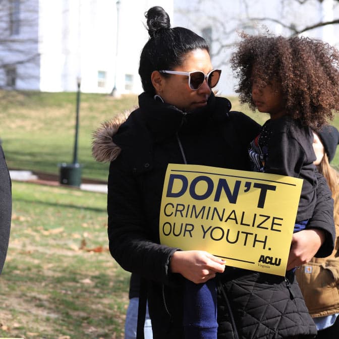 A photo of a protester holding her child and a sign reading "Don`t criminalize our youth."