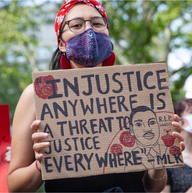 A photo of a protester holding a sign reading 'Injustice anywhere is a threat to justice everywhere - MLK.'