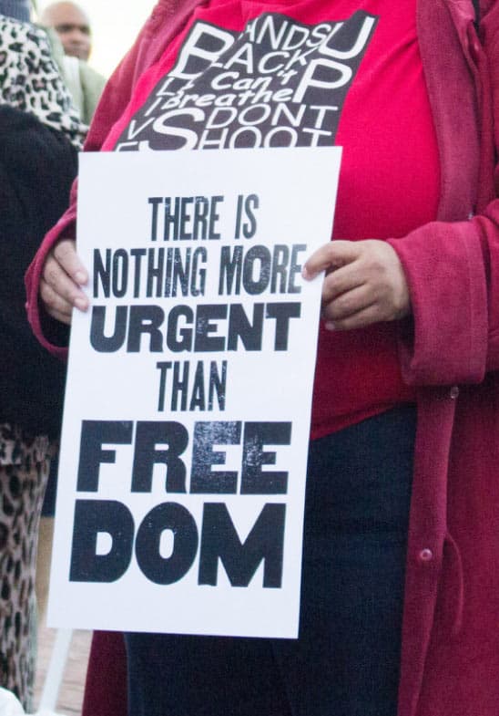 A photo of a person holding a sign reading "There is nothing more urgent than freedom."