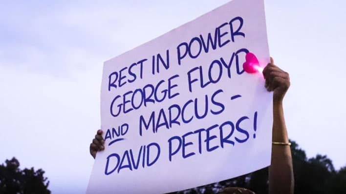A photo of a protest sign reading "Rest in power George Floyd and Marcus-David Peters."